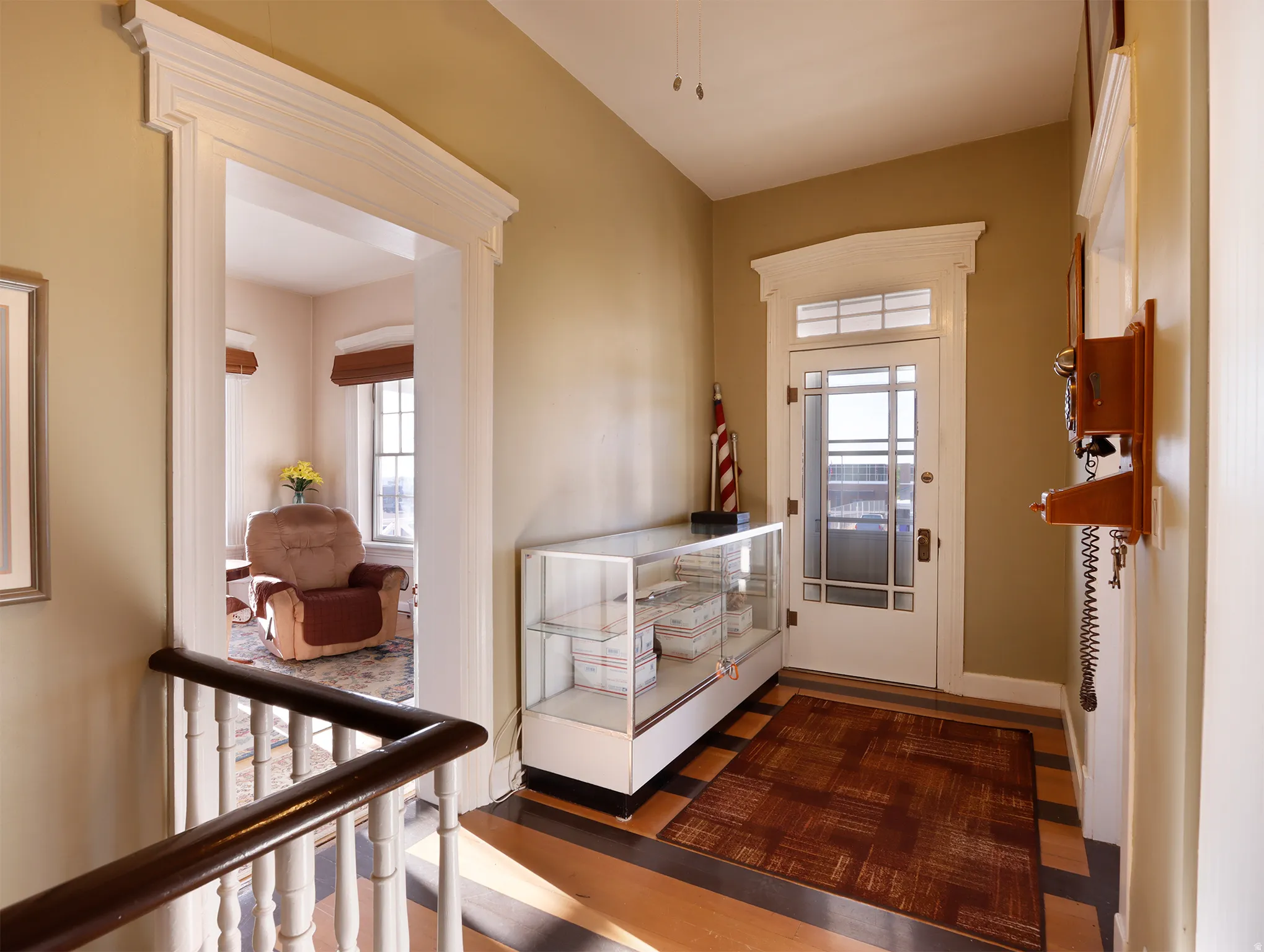 Hallway featuring wood-finish flooring with dark contrasting border, white door casing, and a white front door with transom window