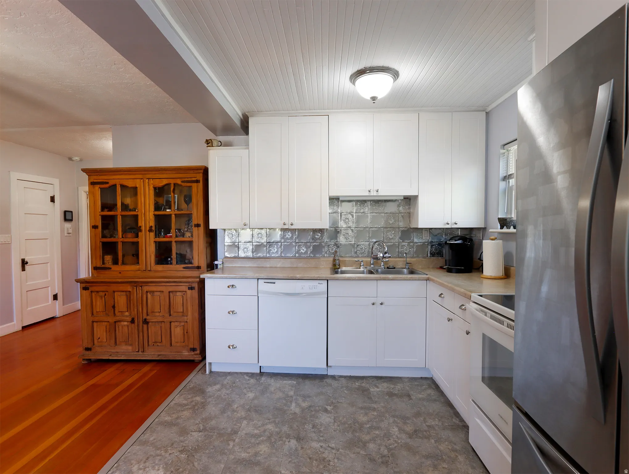 Kitchen featuring white cabinetry, textured backsplash, and contrasting flooring