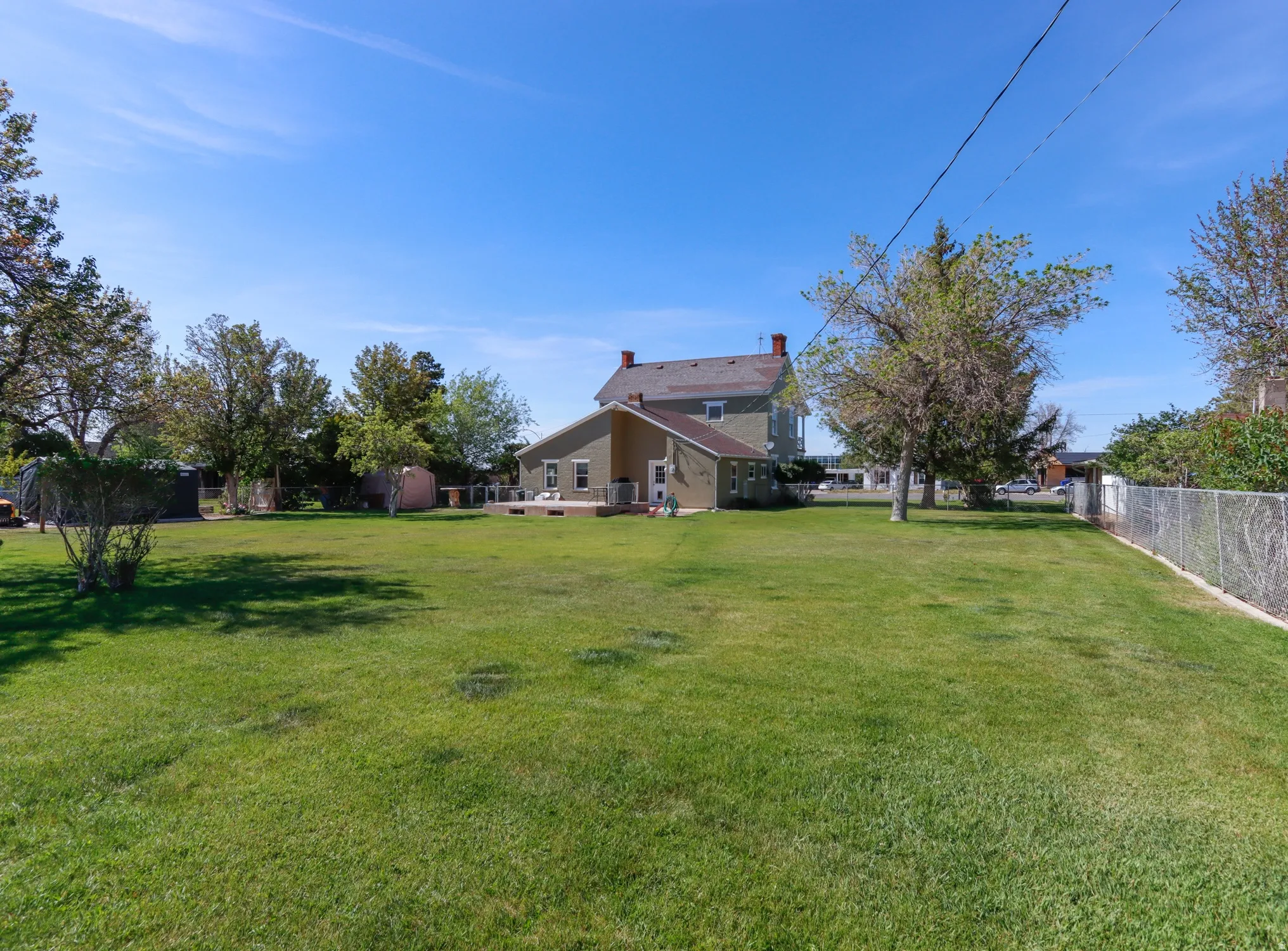 Expansive green lawn with mature trees and a chain-link fence