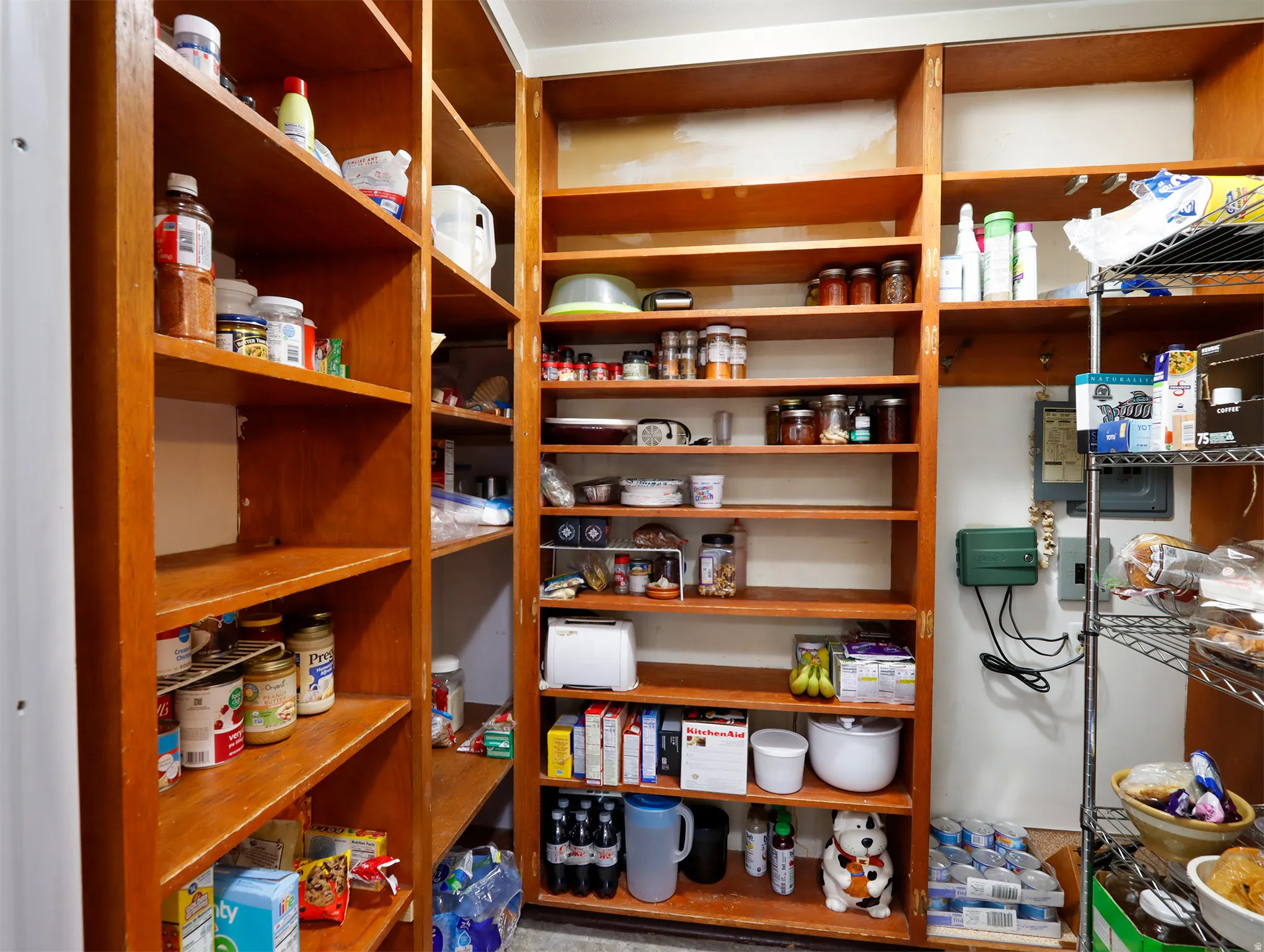 Extensive pantry featuring built-in wooden shelving, additional metal wire shelving, and overhead lighting