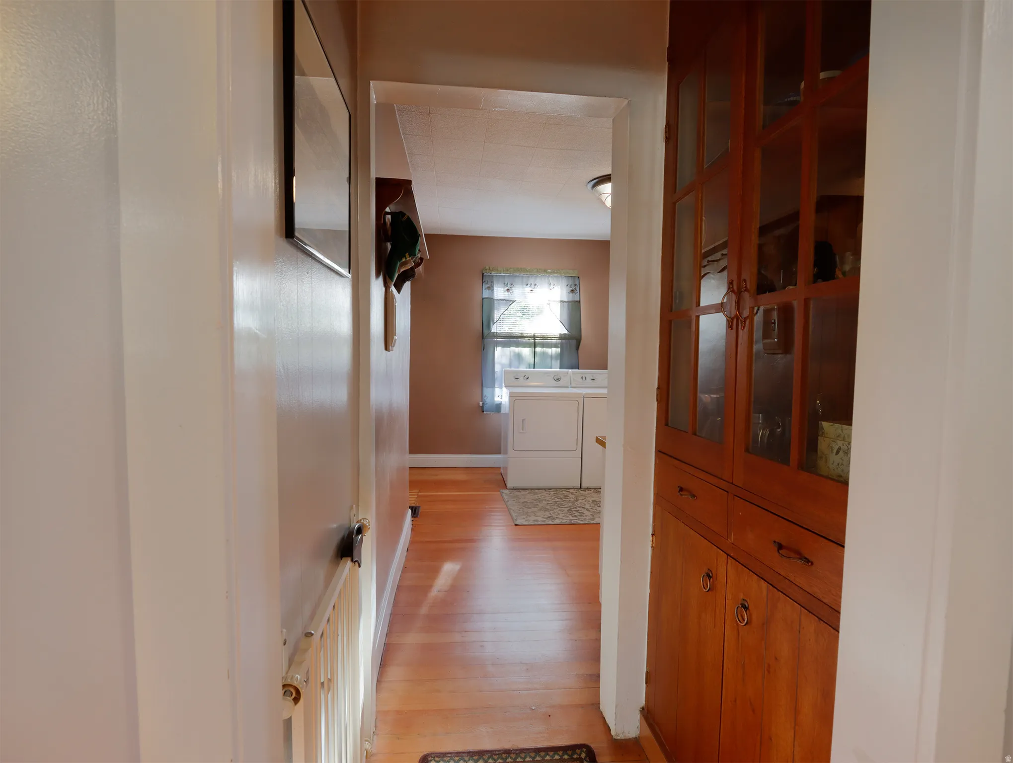 Hallway featuring wood-finish flooring, built-in cabinetry with glass-paneled doors, and a window providing natural light