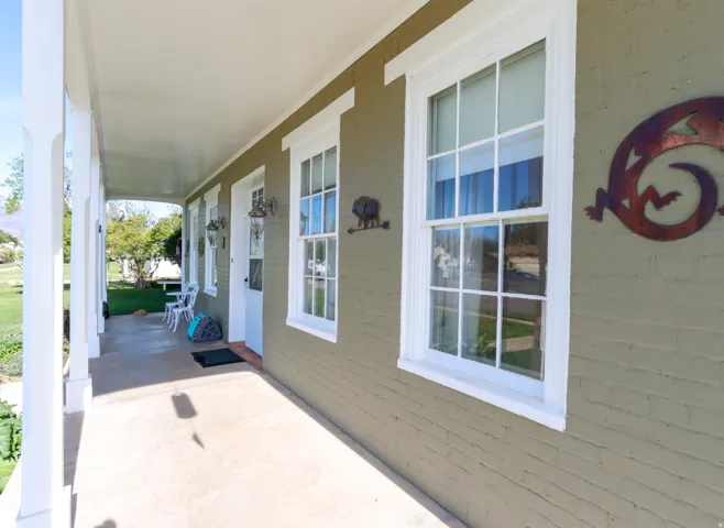 Covered front porch featuring a painted brick exterior, multiple double-hung windows with white trim, and a white front door