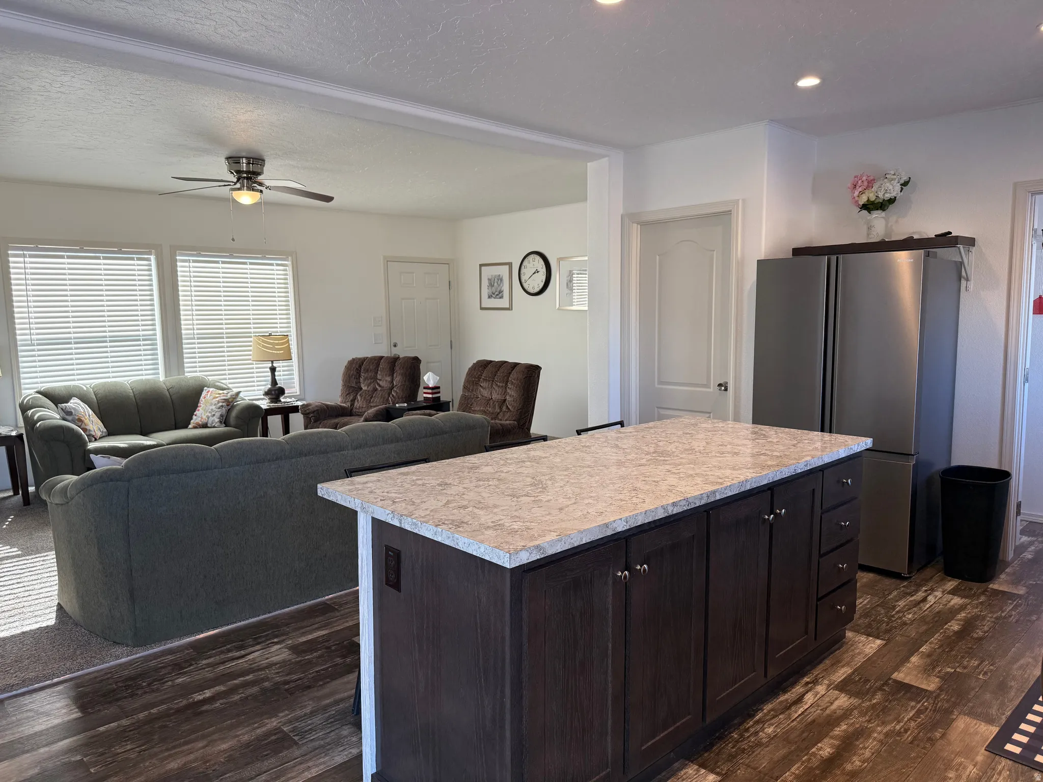 Kitchen featuring light countertops, dark brown cabinets, a center island, freestanding refrigerator, and a textured ceiling