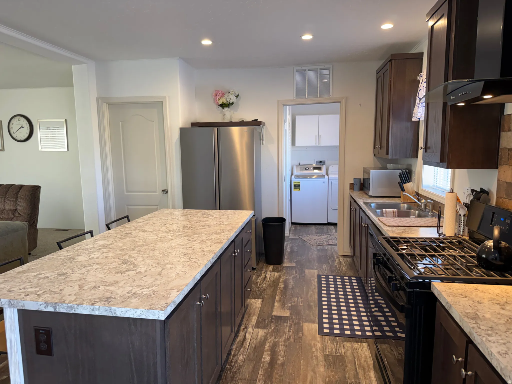 Kitchen featuring dark brown cabinets, gas stove, wall chimney range hood, a kitchen island, and recessed lighting