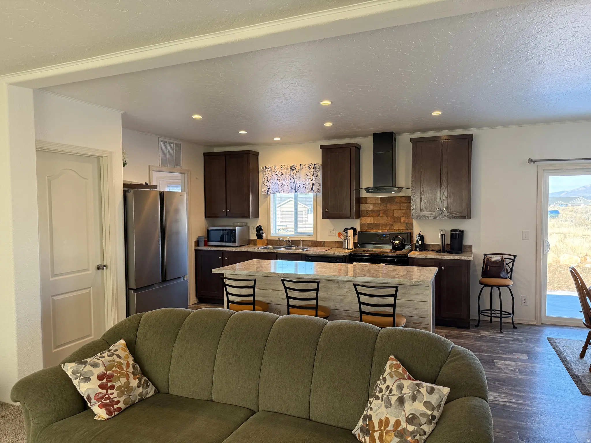 Kitchen with open floor plan, dark brown cabinetry, stainless steel appliances, wall chimney exhaust hood, and a kitchen island