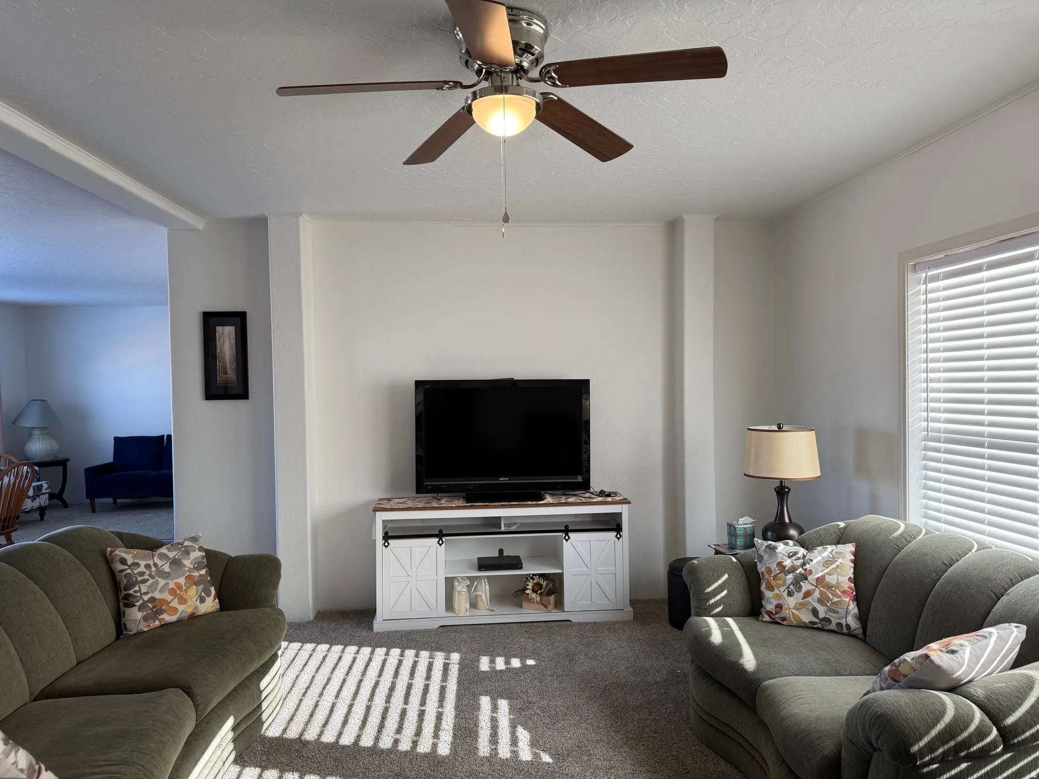 Carpeted living area featuring ceiling fan and a textured ceiling