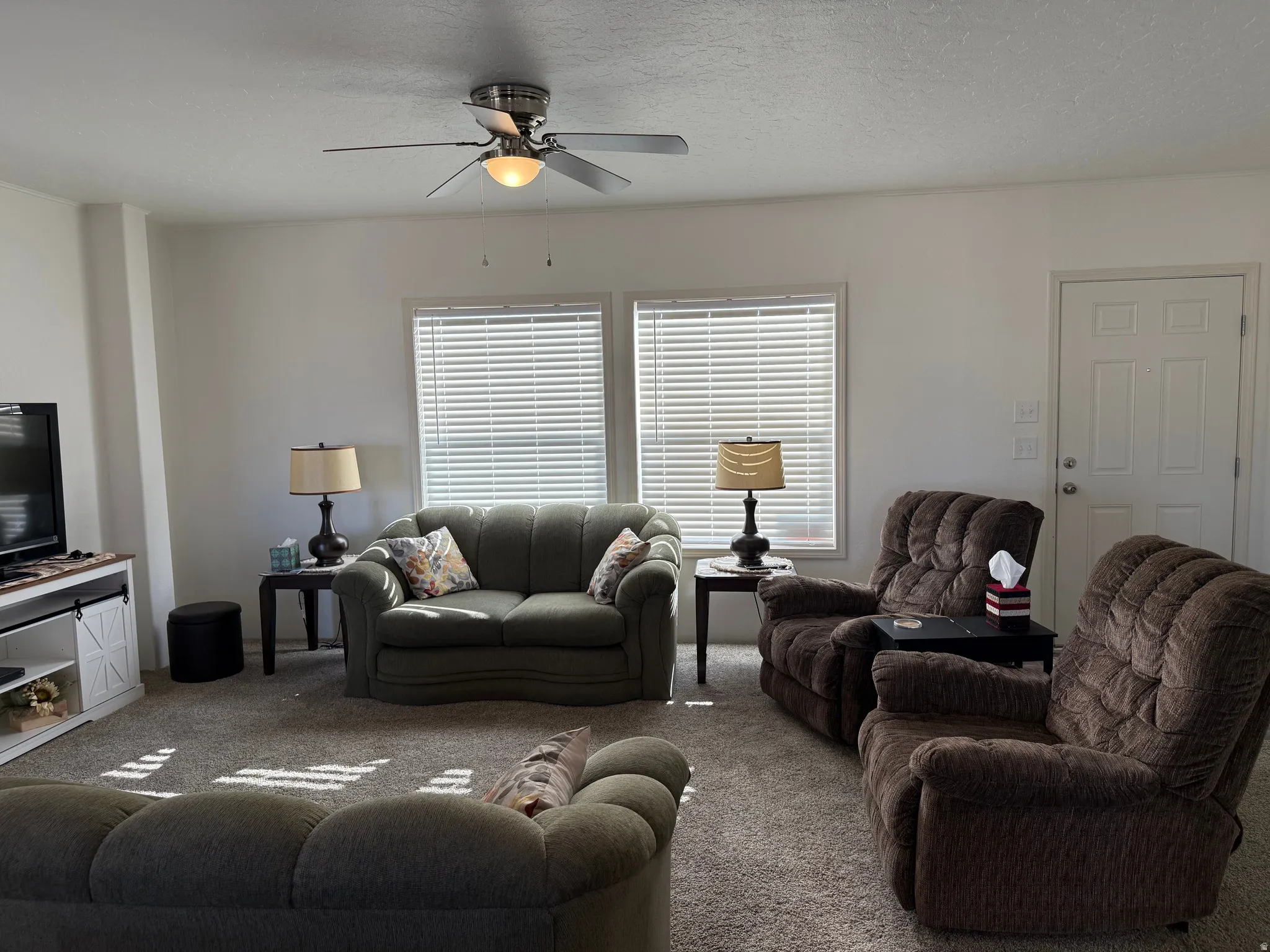Carpeted living room with a ceiling fan and a textured ceiling