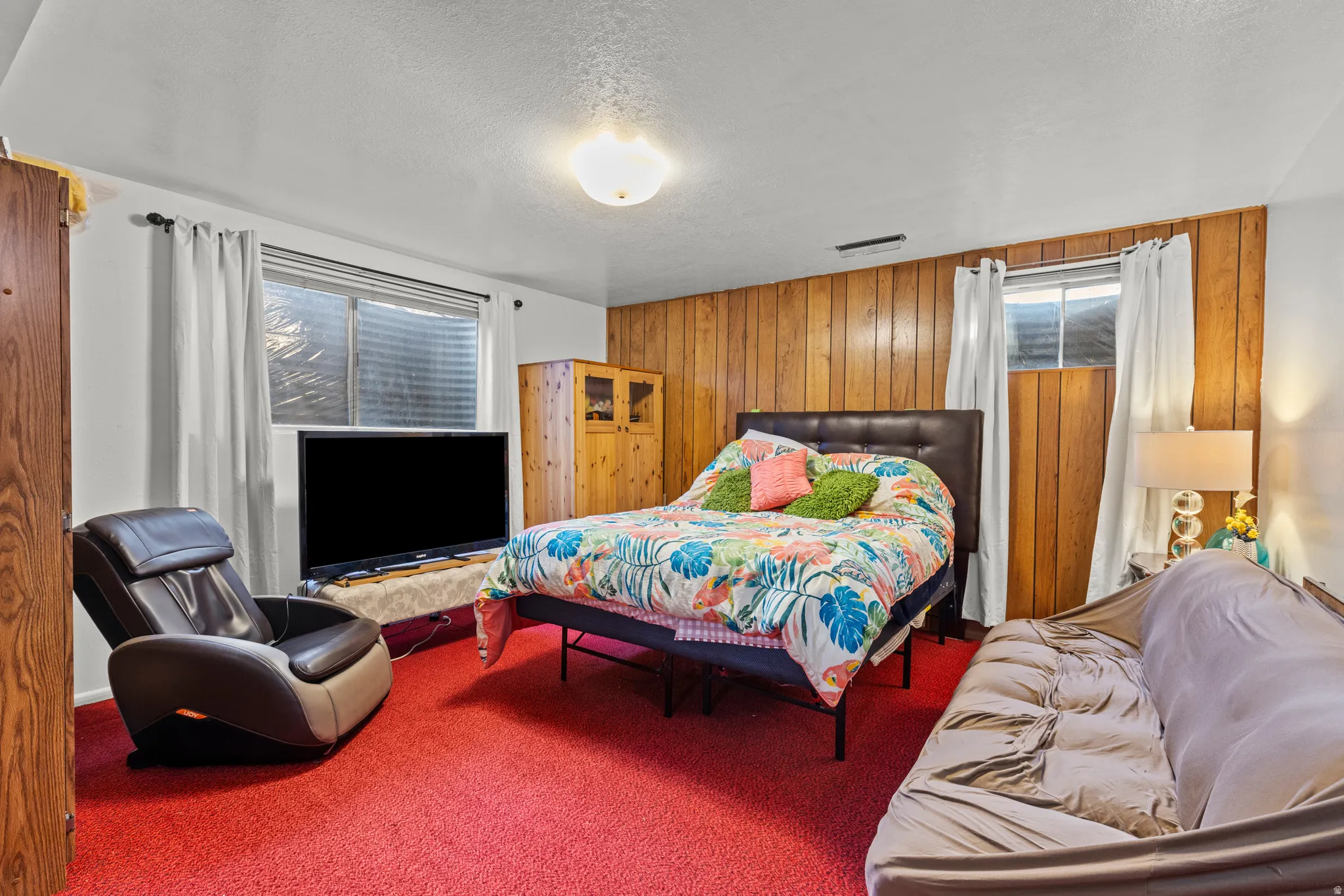 Carpeted bedroom with wood walls, multiple windows, and a textured ceiling