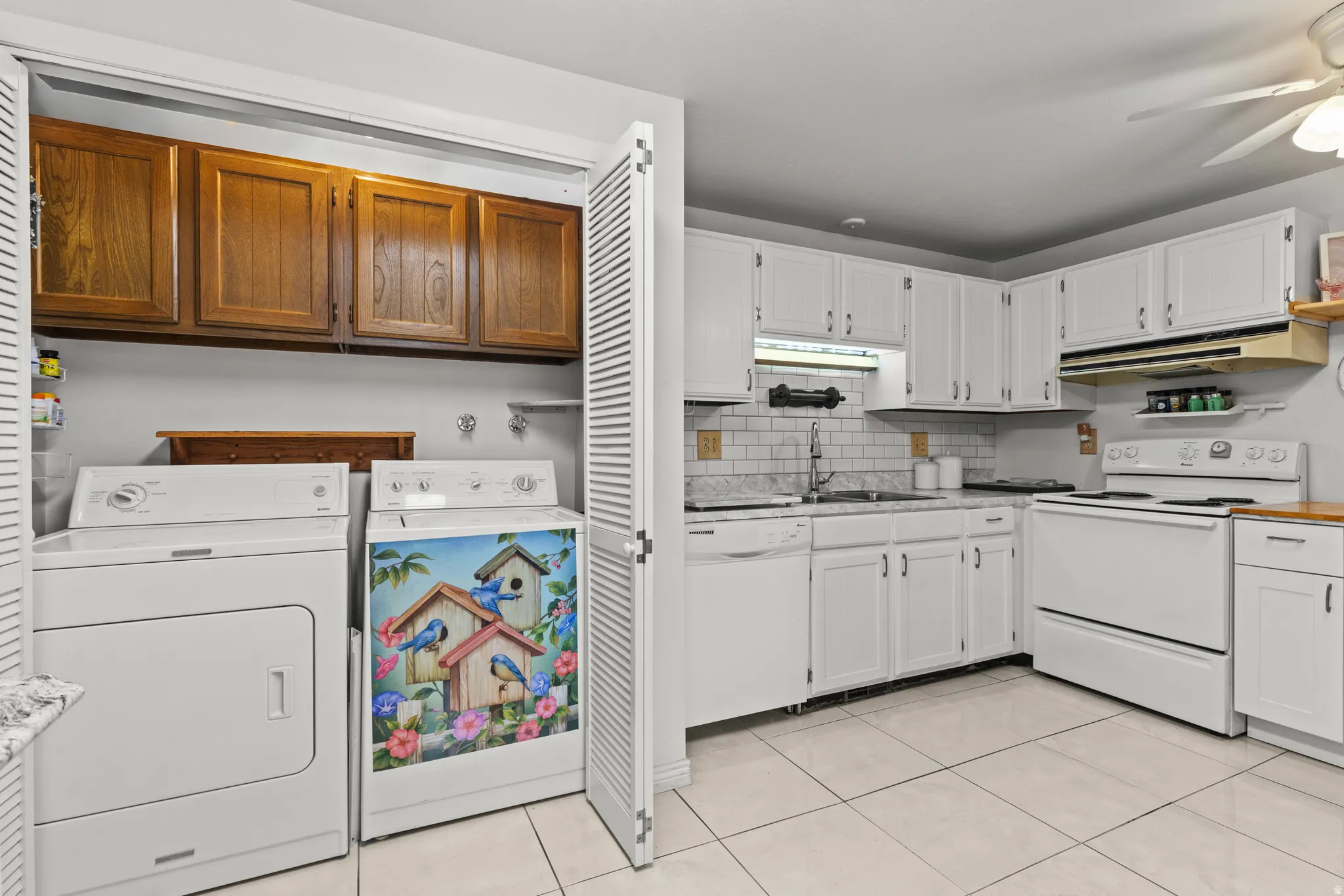 Kitchen with white appliances, decorative backsplash, under cabinet range hood, a ceiling fan, and light tile patterned floors