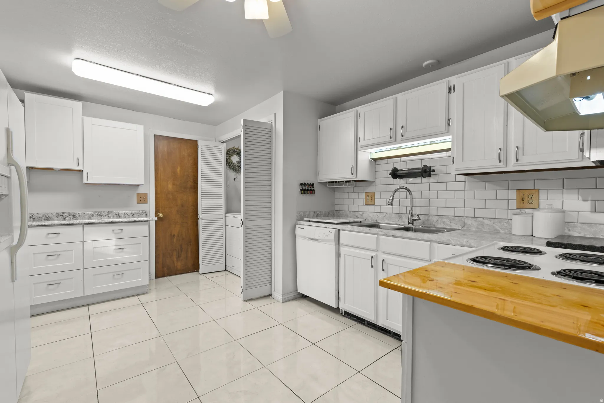 Kitchen featuring under cabinet range hood, white appliances, and white cabinets