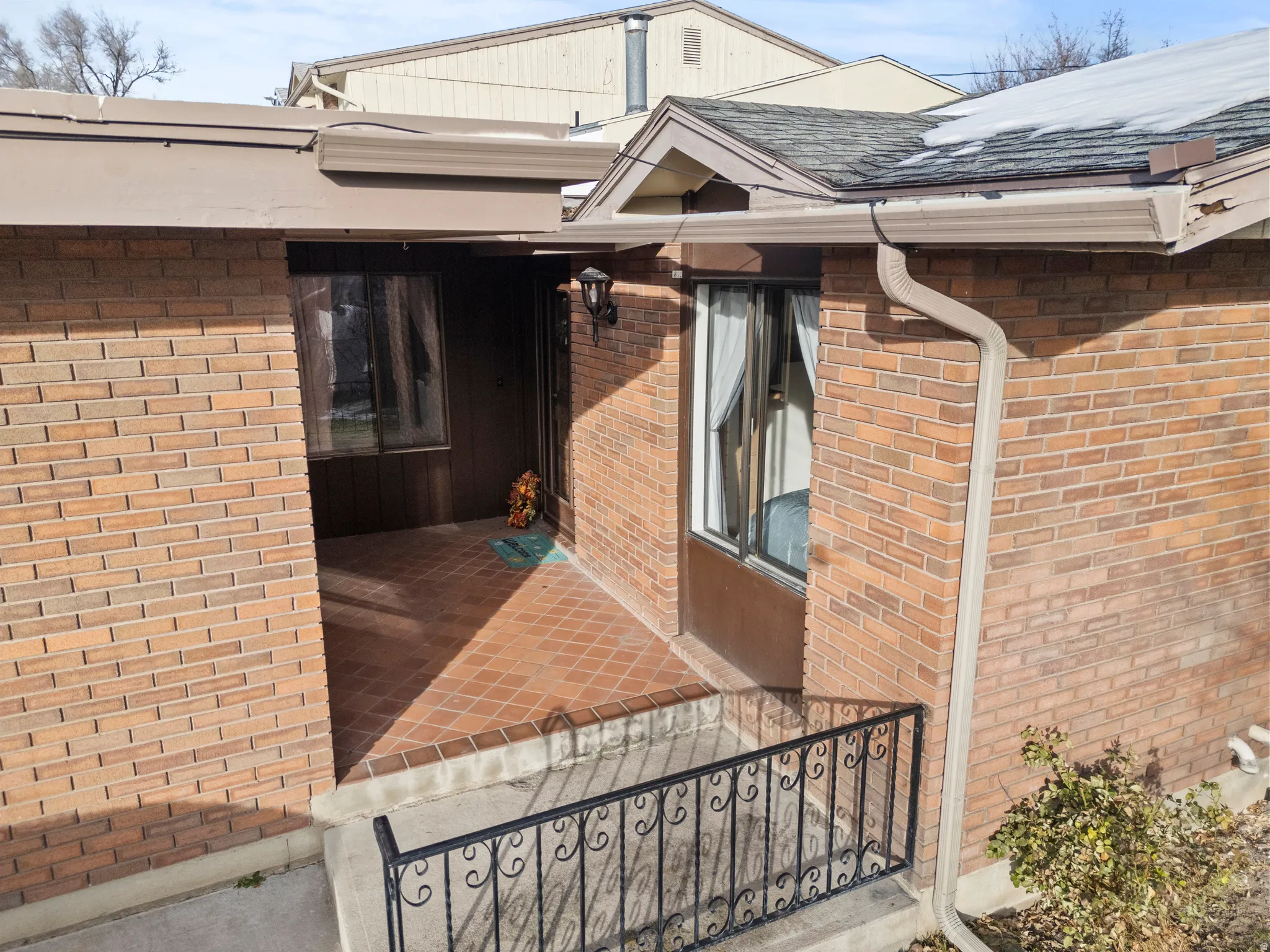 View of exterior entry with brick siding and a shingled roof