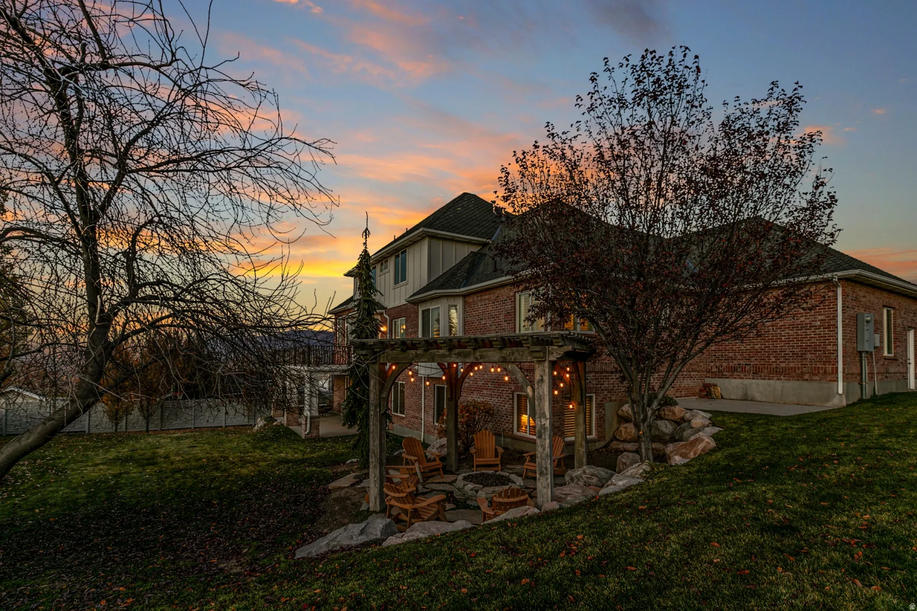 Back of property at dusk with brick siding, a lawn, a pergola, and a patio area