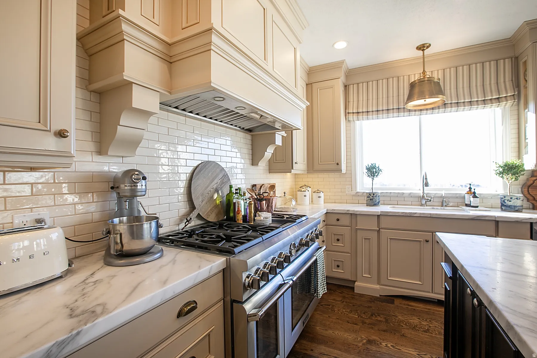 Kitchen featuring range with two ovens, cream cabinets, dark wood finished floors, pendant lighting, and light stone countertops