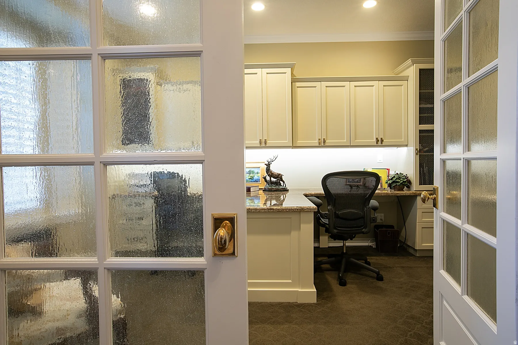Home office with built in study area, crown molding, and dark colored carpet
