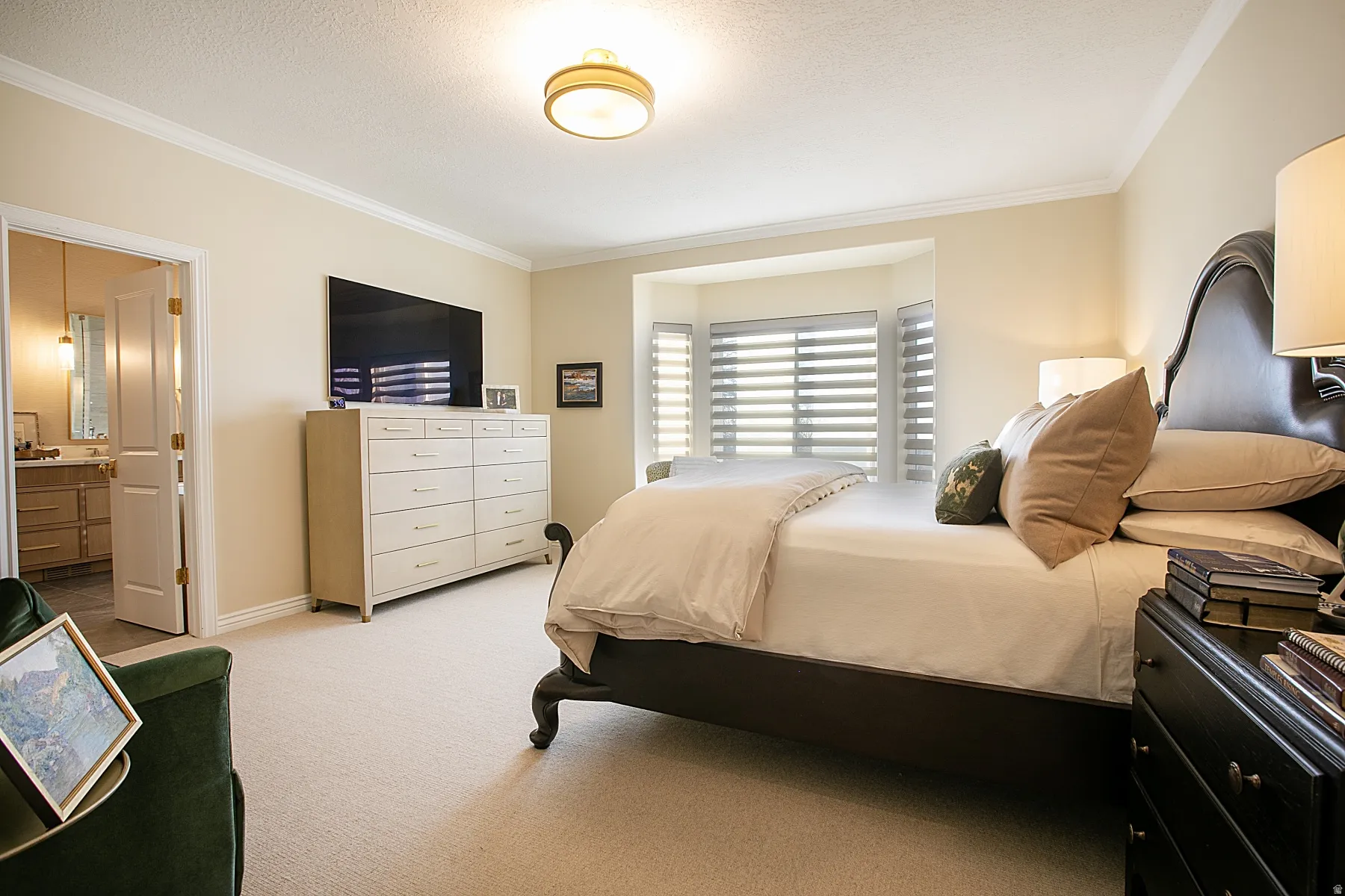 Bedroom featuring crown molding, light carpet, ensuite bathroom, and a textured ceiling