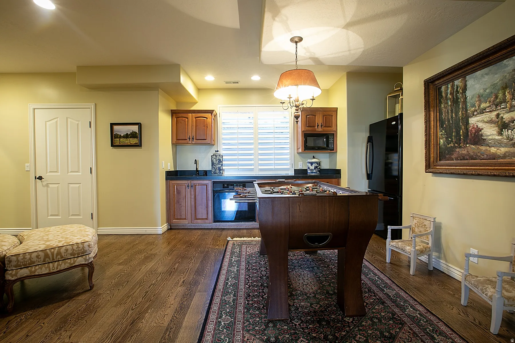 Kitchen featuring dark countertops, black appliances, brown cabinets, hanging light fixtures, and dark wood-style flooring