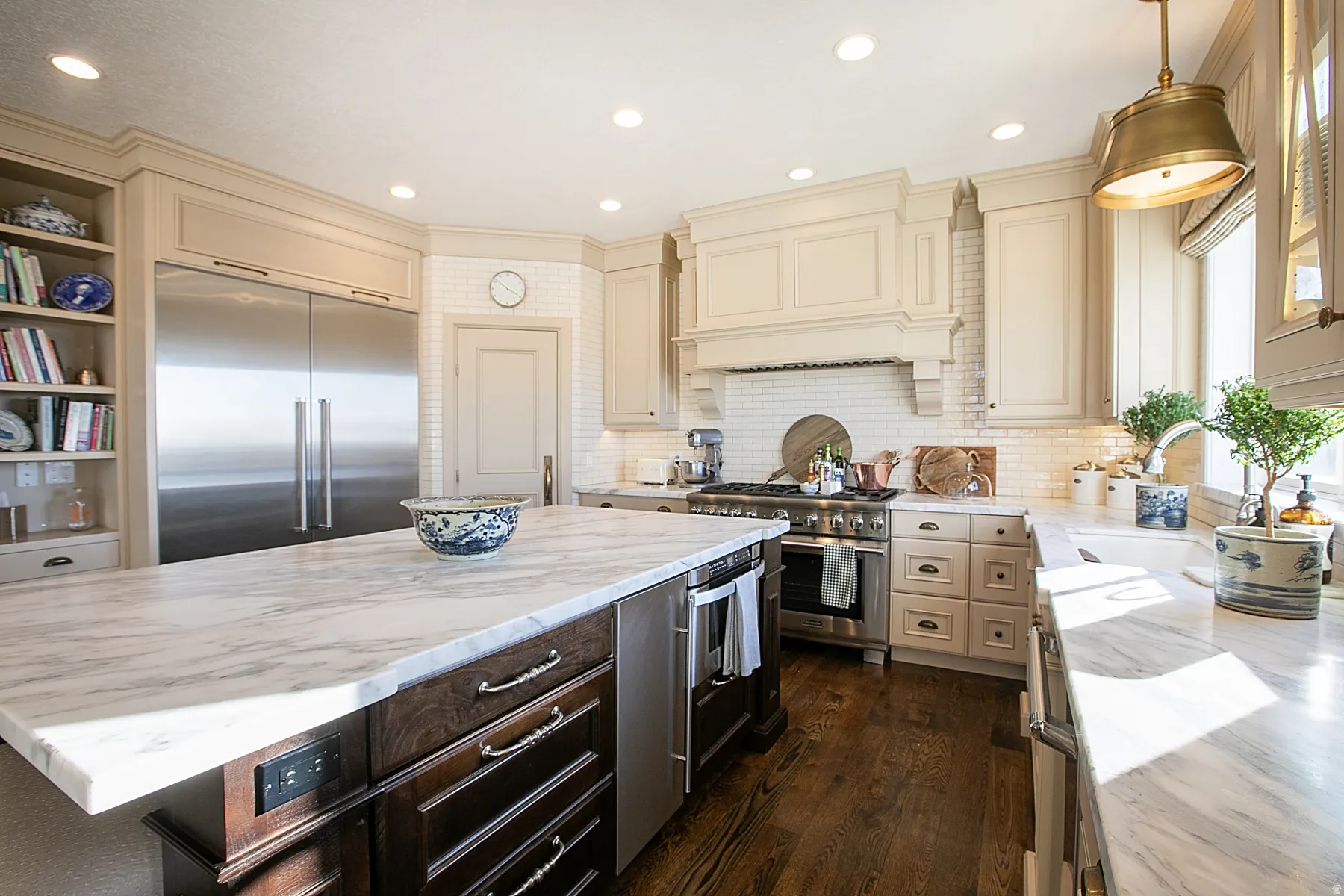 Kitchen featuring cream cabinetry, premium appliances, marble counters, hanging light fixtures, and a kitchen island