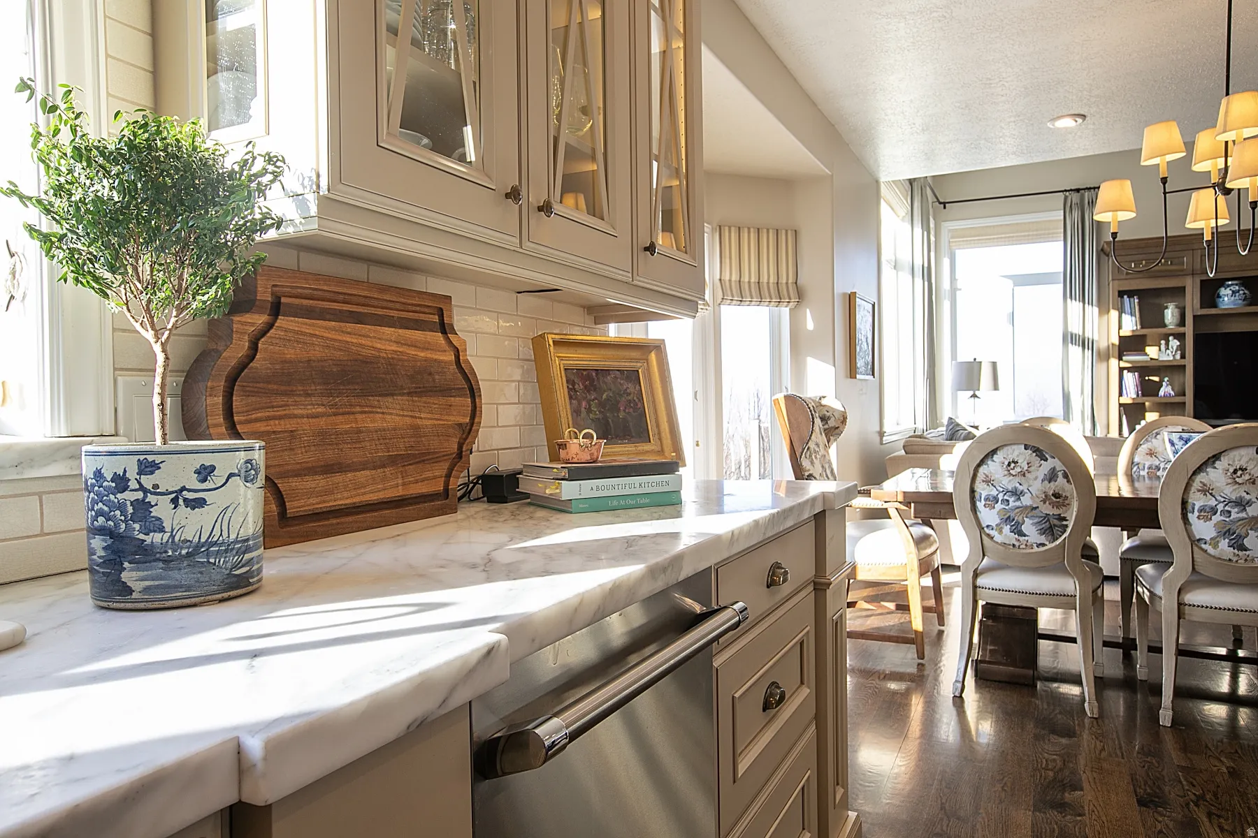 Kitchen with glass insert cabinets, light stone countertops, dishwasher, cream cabinets, and decorative light fixtures