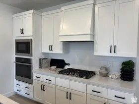 Kitchen featuring custom exhaust hood, white cabinetry, stainless steel oven, and built in microwave