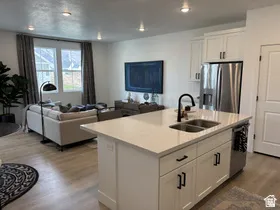 Kitchen featuring open floor plan, white cabinets, stainless steel appliances, an island with sink, and wood finished floors