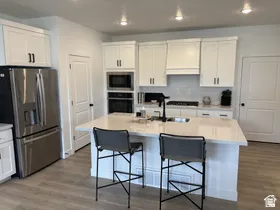Kitchen with appliances with stainless steel finishes, white cabinets, dark wood-type flooring, recessed lighting, and a kitchen island with sink