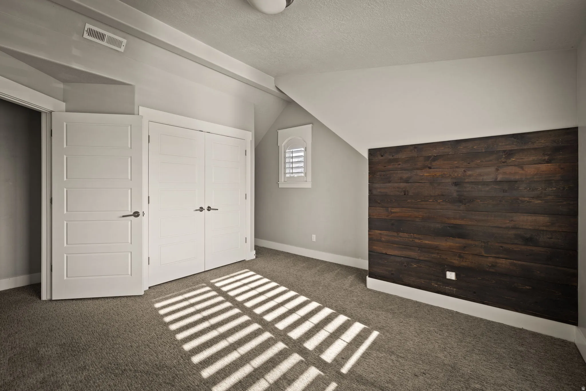 Unfurnished bedroom with lofted ceiling, a textured ceiling, a closet, and dark carpet