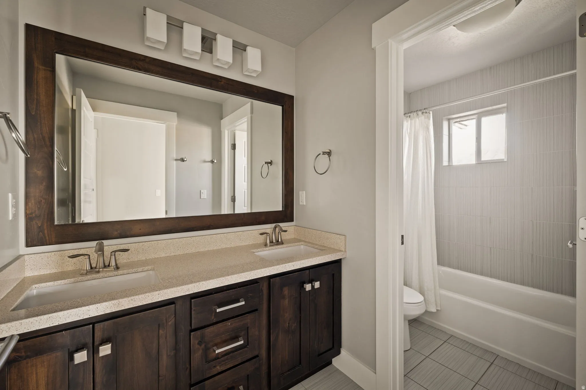 Bathroom featuring shower / tub combo with curtain, double vanity, and light tile patterned flooring