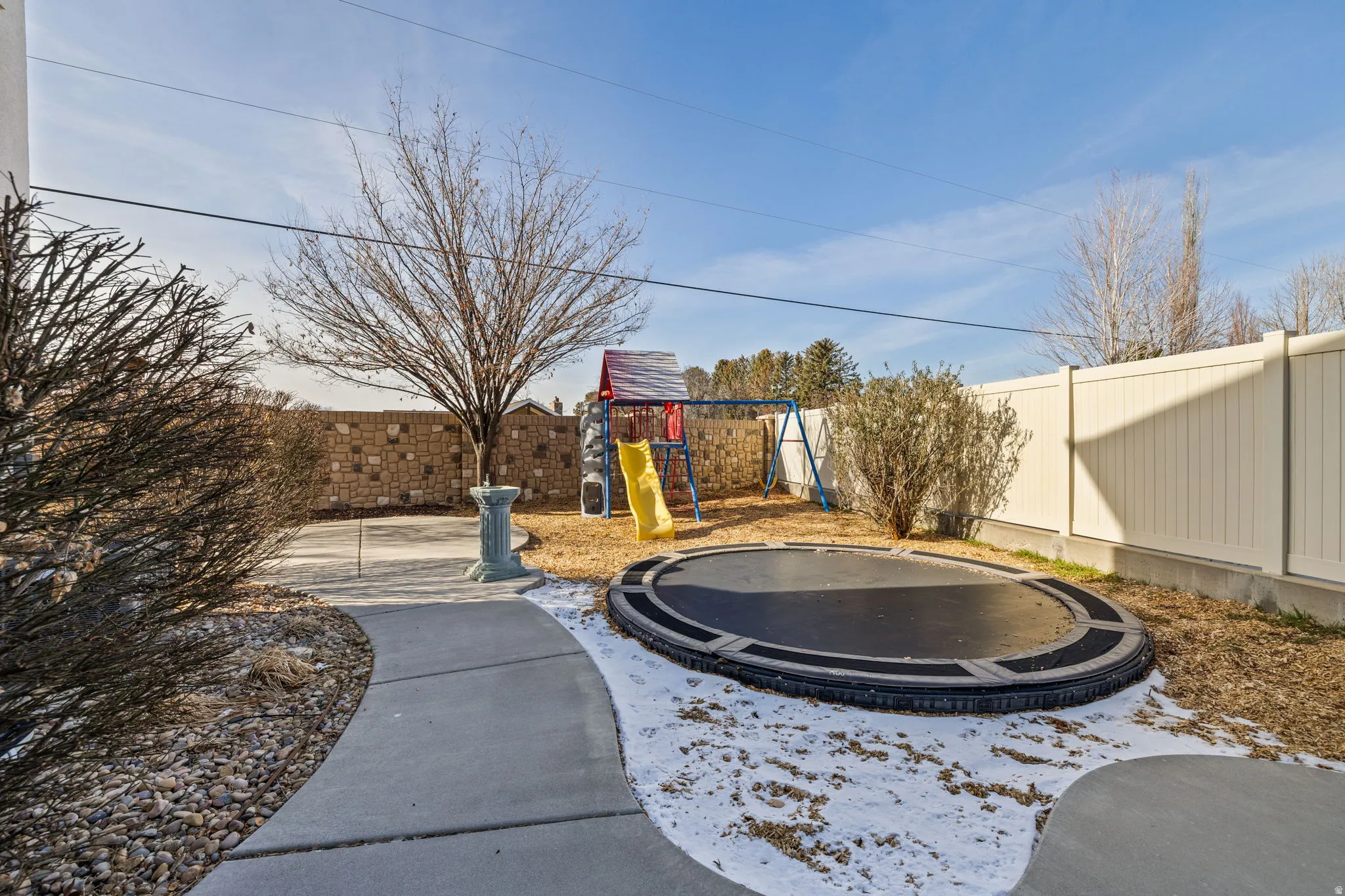Fenced backyard featuring a playground and a trampoline