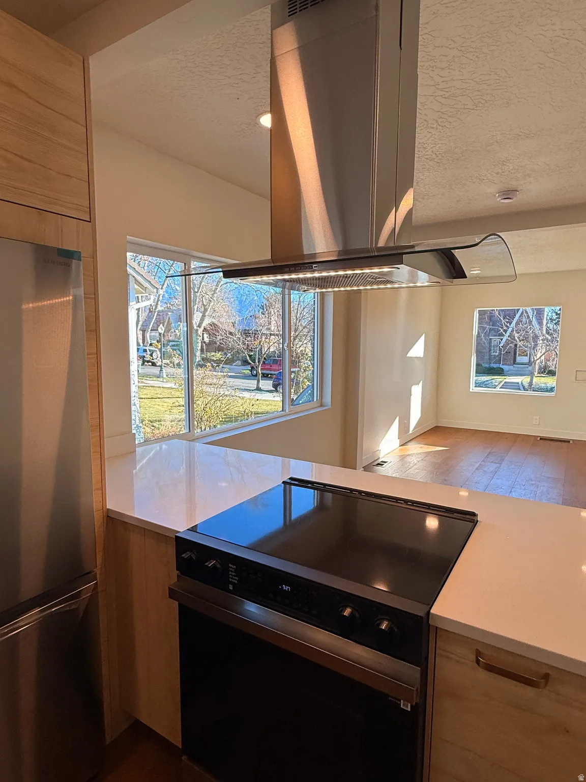 Kitchen featuring island exhaust hood, black electric range, freestanding refrigerator, a textured ceiling, and dark wood-style floors