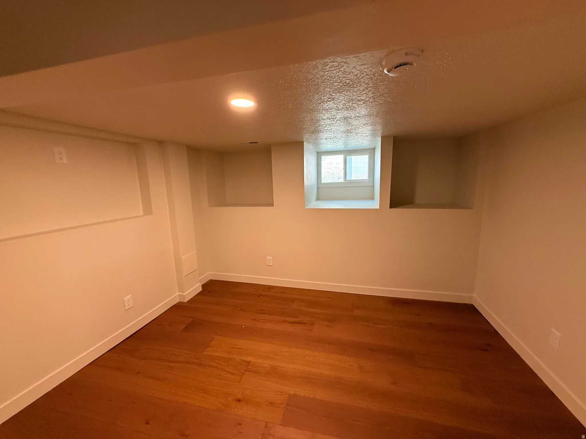 Below grade area featuring a textured ceiling, dark wood-type flooring, and recessed lighting