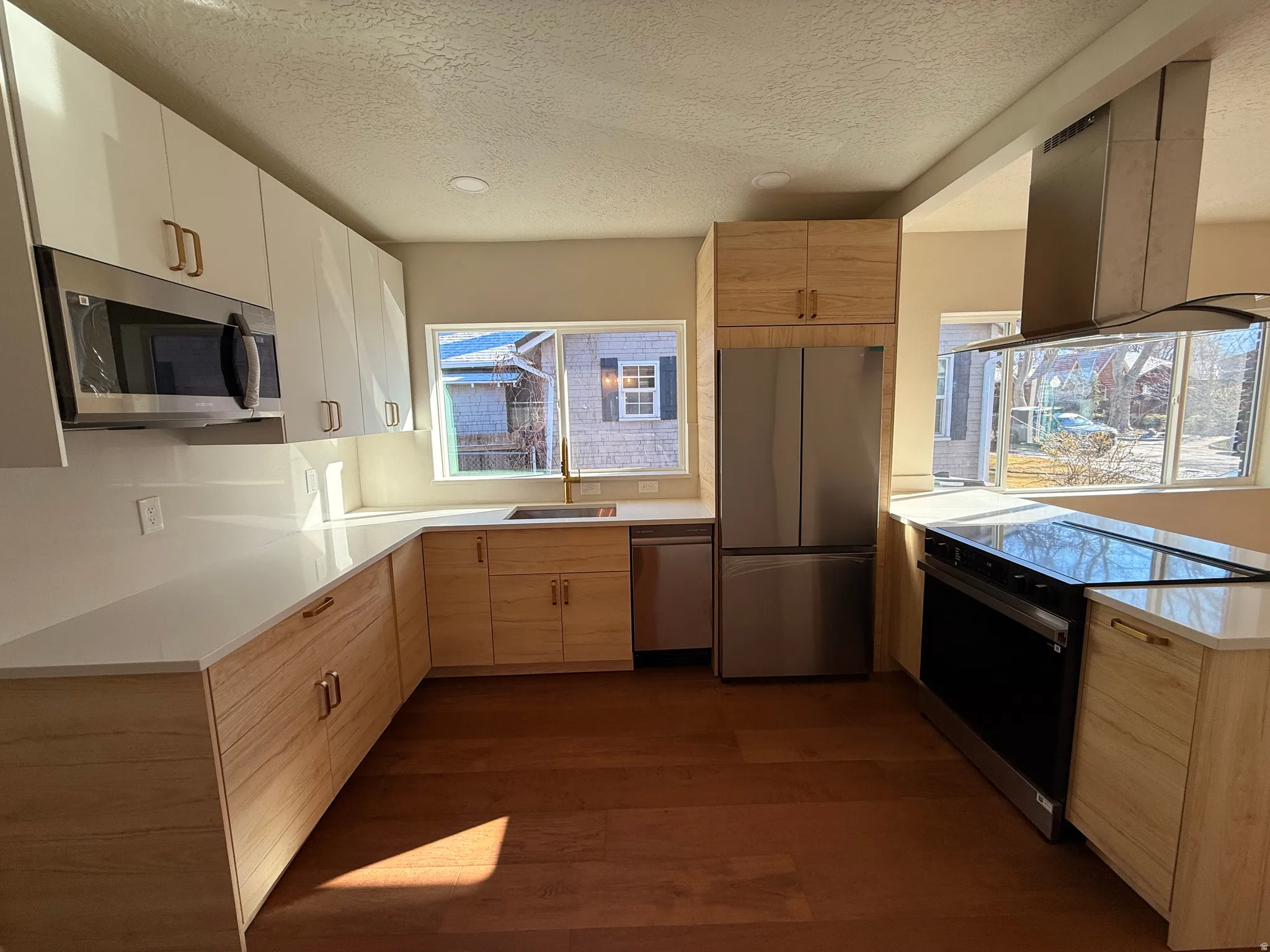 Kitchen featuring stainless steel appliances, exhaust hood, a peninsula, a textured ceiling, and light brown cabinets