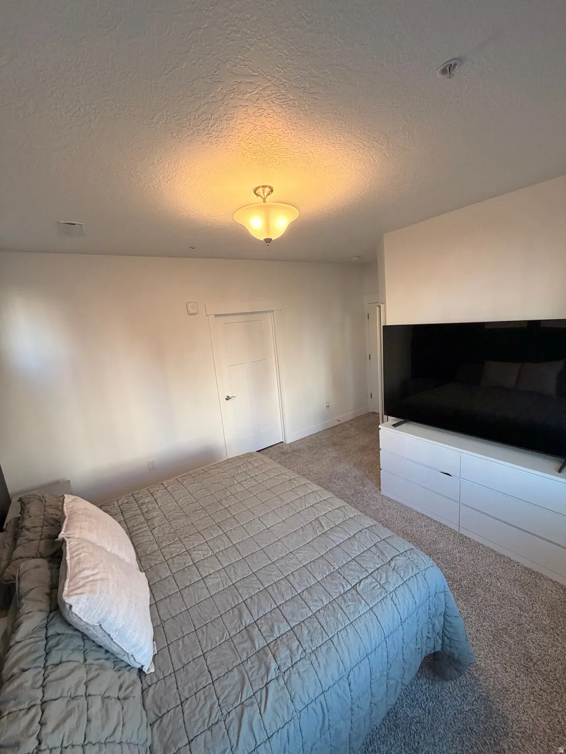 Carpeted bedroom featuring a textured ceiling and baseboards