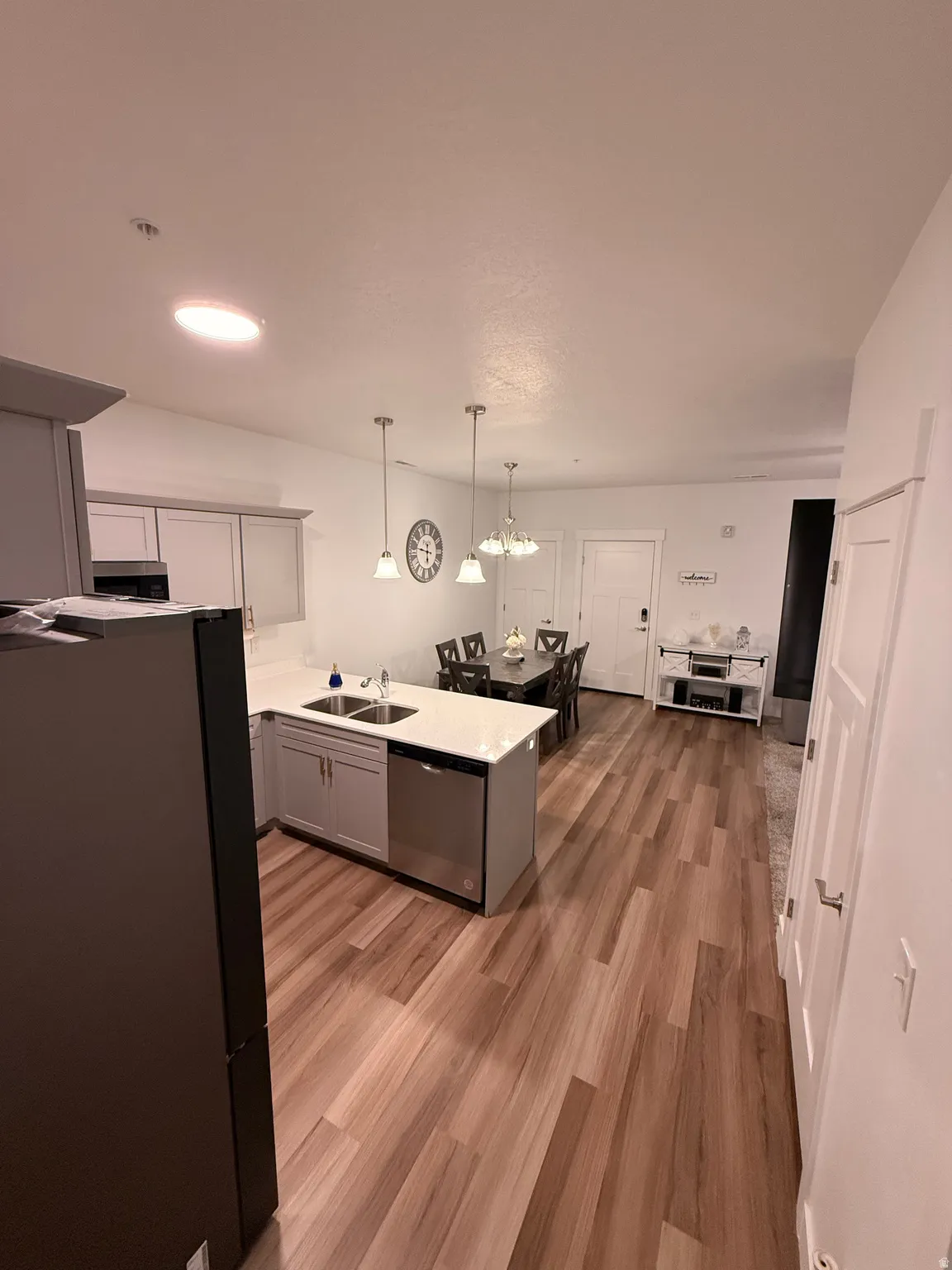 Kitchen featuring a peninsula, hanging light fixtures, light wood-type flooring, appliances with stainless steel finishes, and gray cabinetry