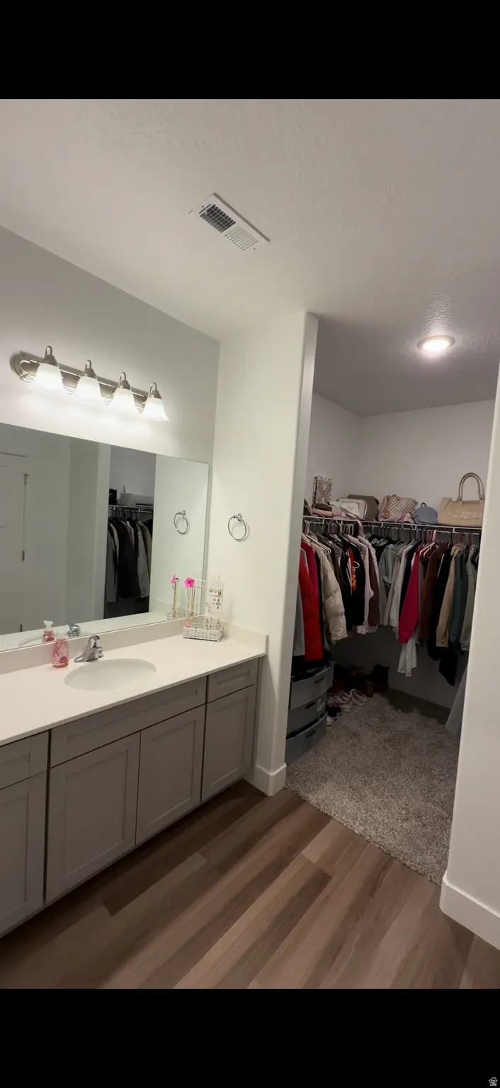 Full bath with a spacious closet, vanity, and dark wood-style floors