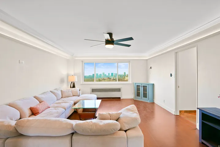 Living area with radiator, a ceiling fan, wood finished floors, and crown molding