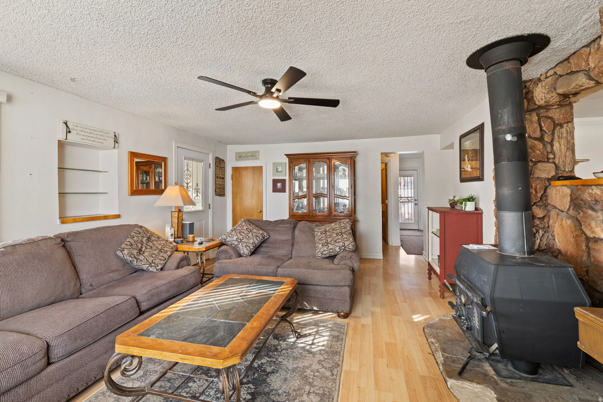 Living room featuring a wood stove, light wood-style flooring, a textured ceiling, and ceiling fan