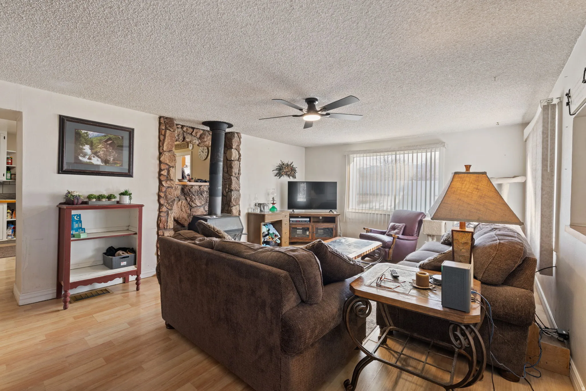 Living area featuring a wood stove, light wood-style floors, a textured ceiling, and a ceiling fan