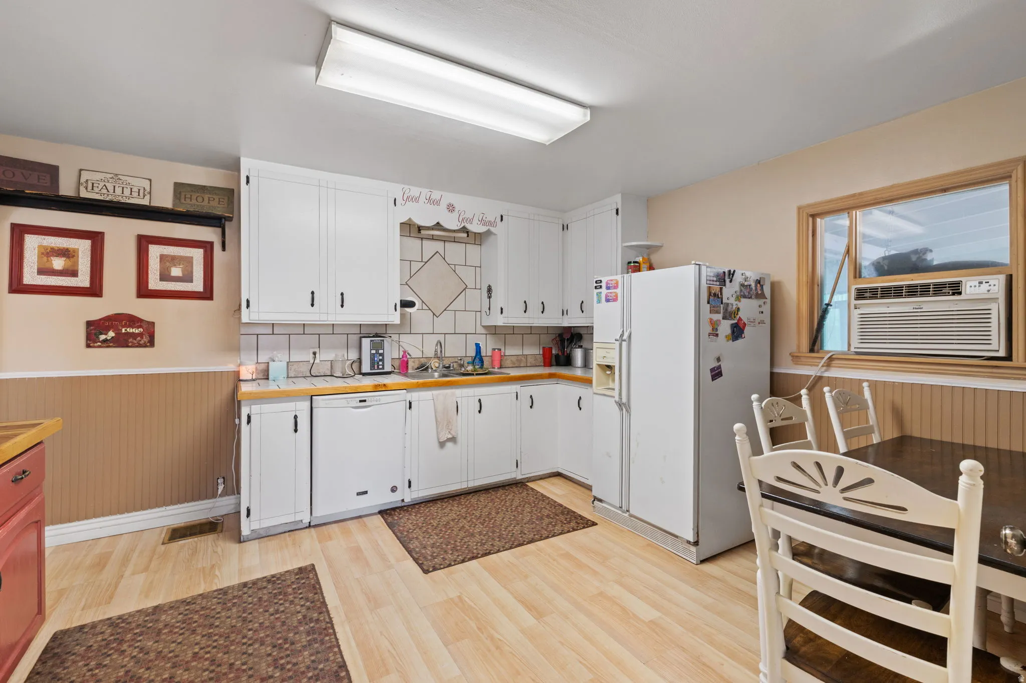 Kitchen with a wainscoted wall, white cabinets, white appliances, light wood finished floors, and tasteful backsplash