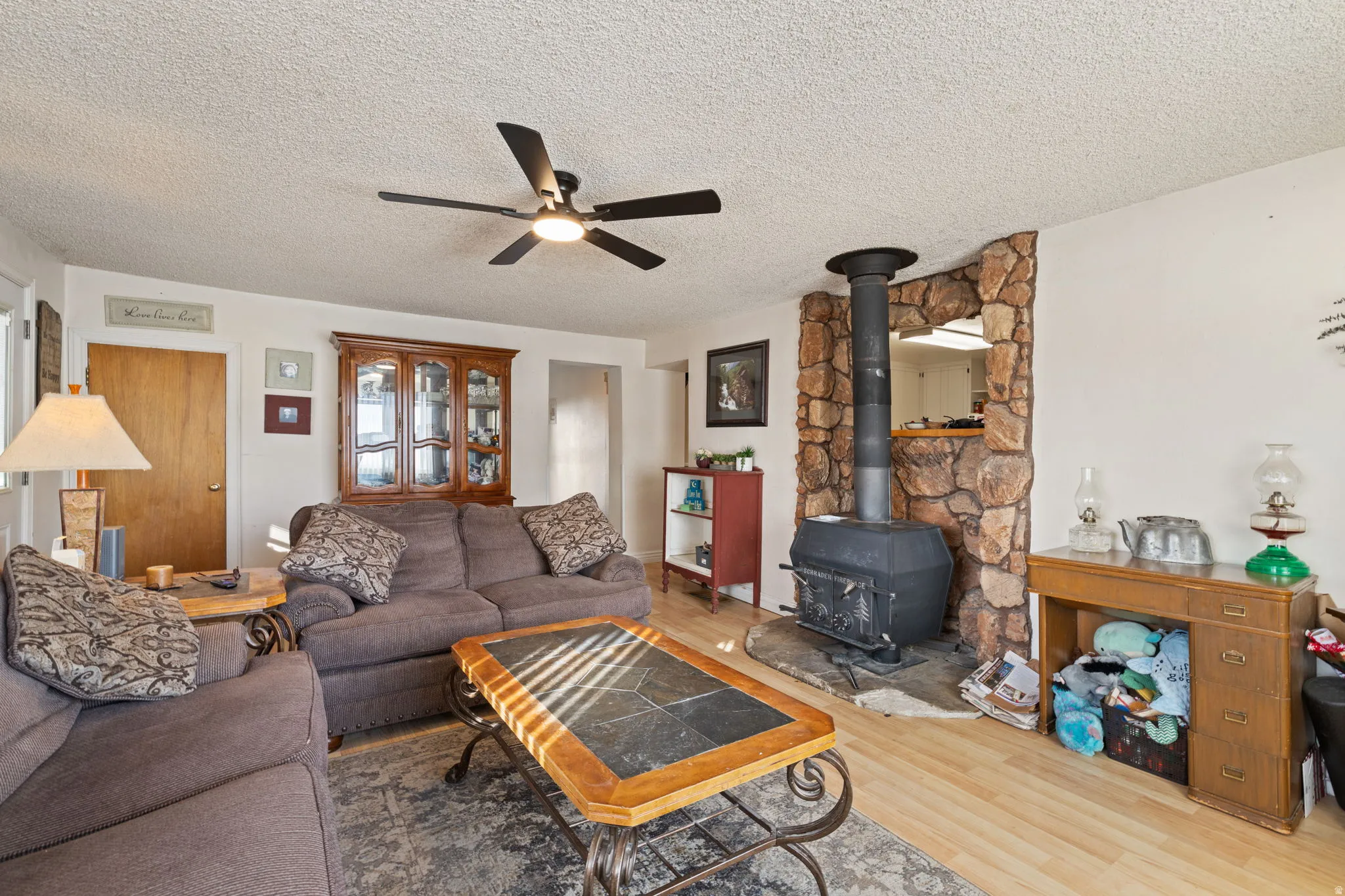 Living room featuring a wood stove, wood finished floors, a ceiling fan, and a textured ceiling