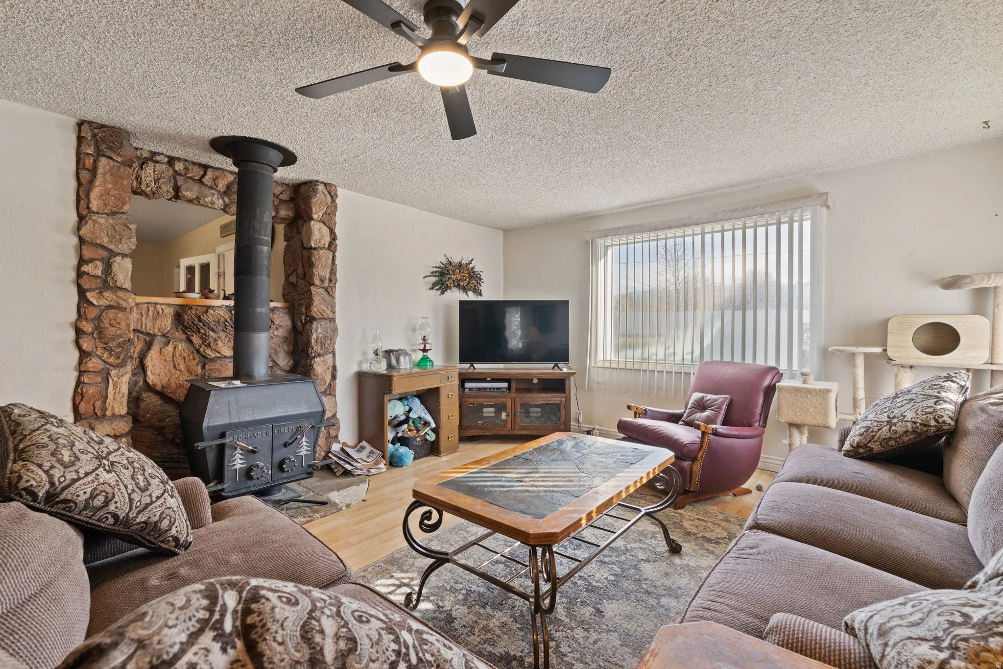 Living area with a wood stove, a textured ceiling, wood finished floors, and ceiling fan