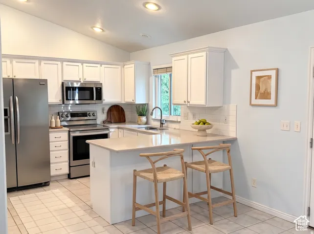 Kitchen featuring white cabinetry, solid surface countertops, a white subway tile backsplash, stainless steel appliances, and tile flooring