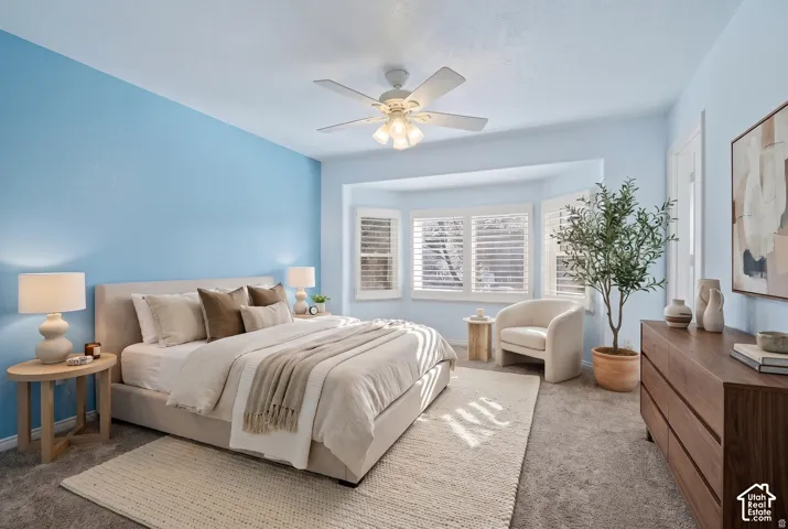 Bedroom featuring neutral carpeting, a bay window with louvered shutters, and a ceiling-mounted light fixture with a fan