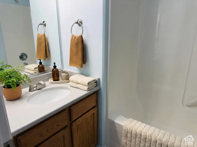 Bathroom vanity featuring wood-finish cabinetry, a white countertop with an integrated oval sink, a wall-mounted mirror, and a tub and shower combination with a white surround