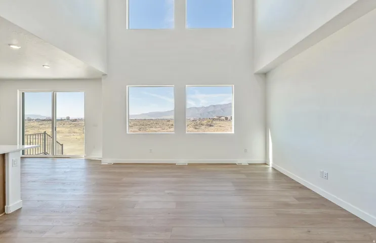 Unfurnished living room featuring healthy amount of natural light, light wood-style floors, and a high ceiling