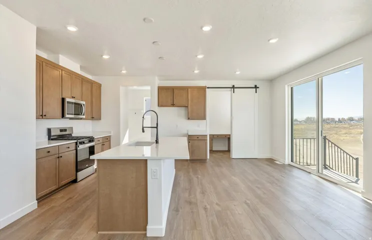 Kitchen featuring a barn door, stainless steel appliances, brown cabinets, recessed lighting, and light wood-style floors