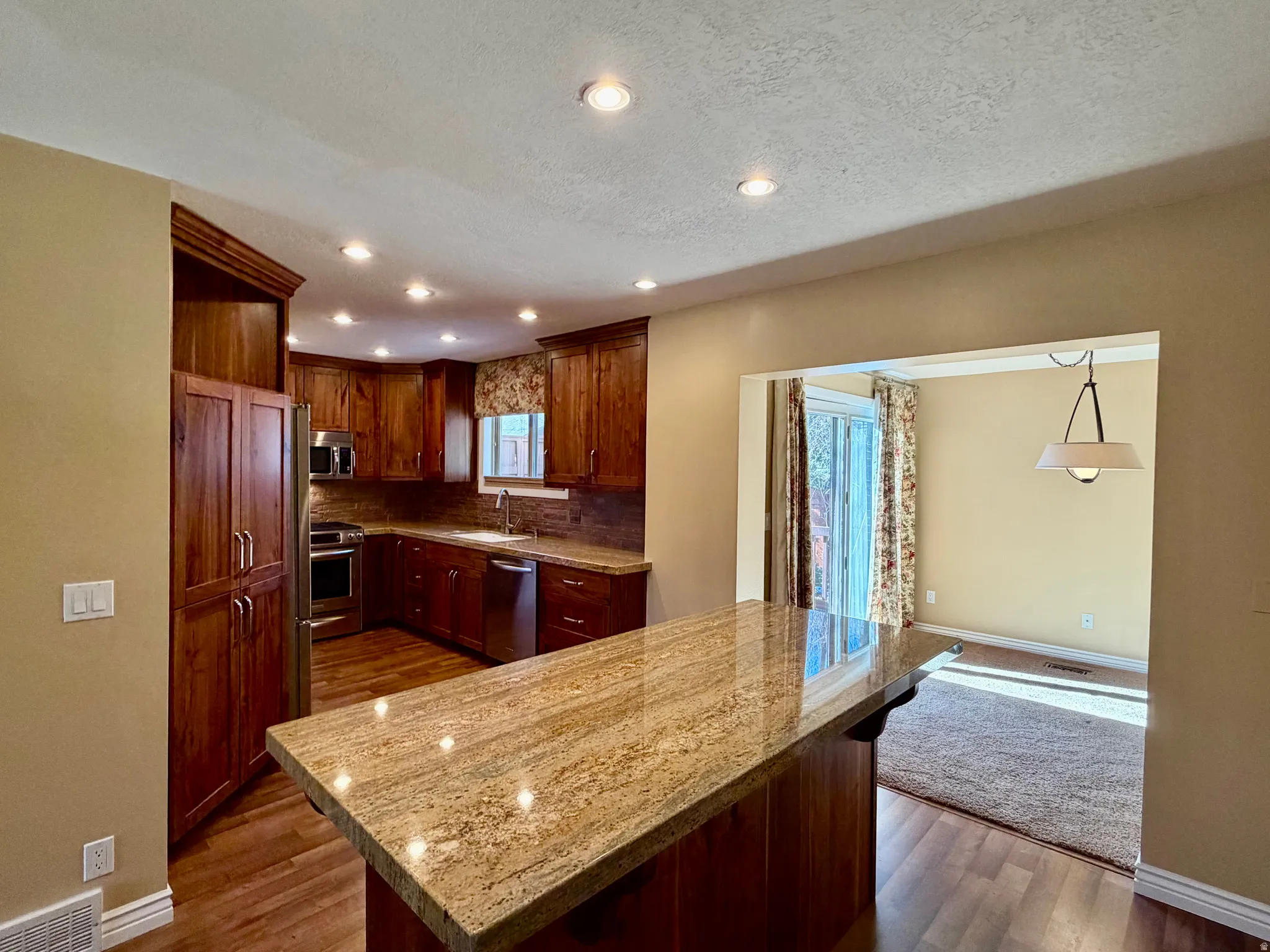 Kitchen featuring appliances with stainless steel finishes, recessed lighting, dark wood-type flooring, light stone countertops, and open floor plan