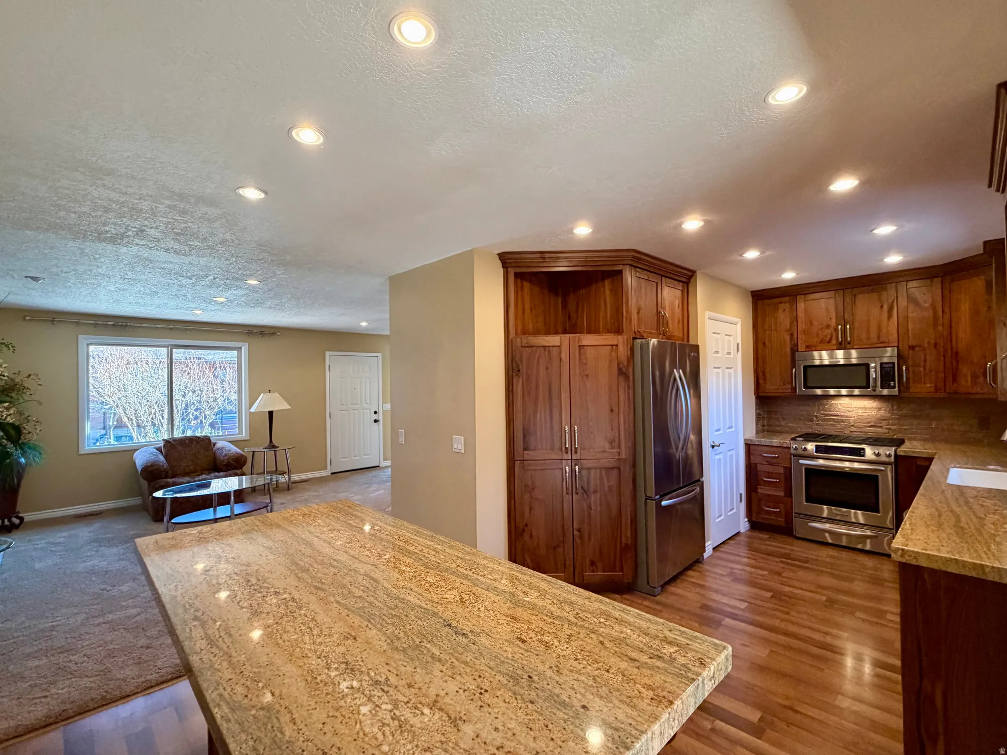 Kitchen featuring open floor plan, appliances with stainless steel finishes, a textured ceiling, tasteful backsplash, and recessed lighting