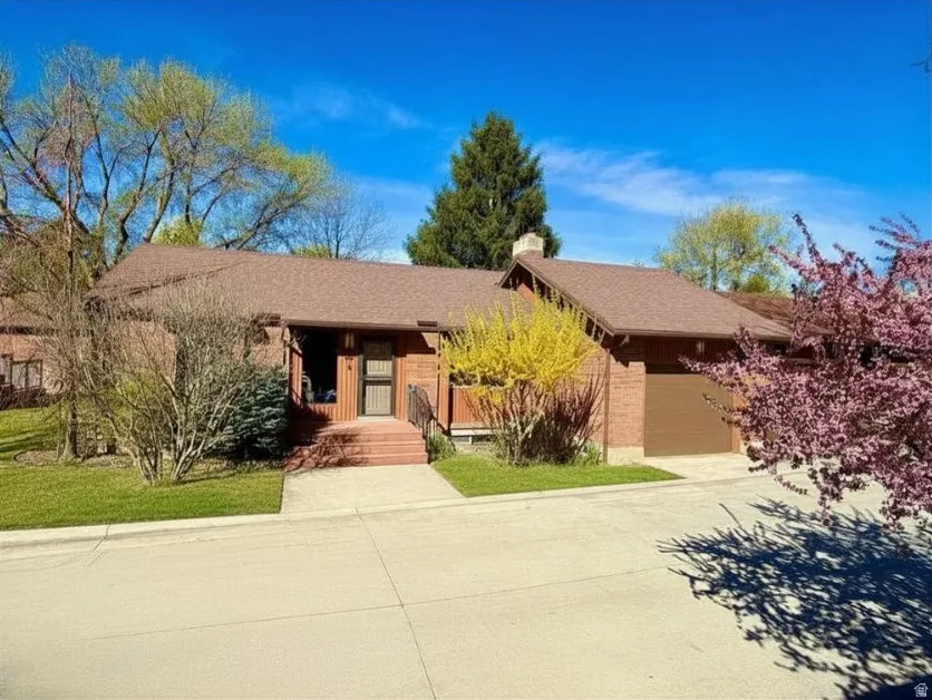 Ranch-style house featuring attractive landscaping, an attached garage, driveway, a chimney, and a porch