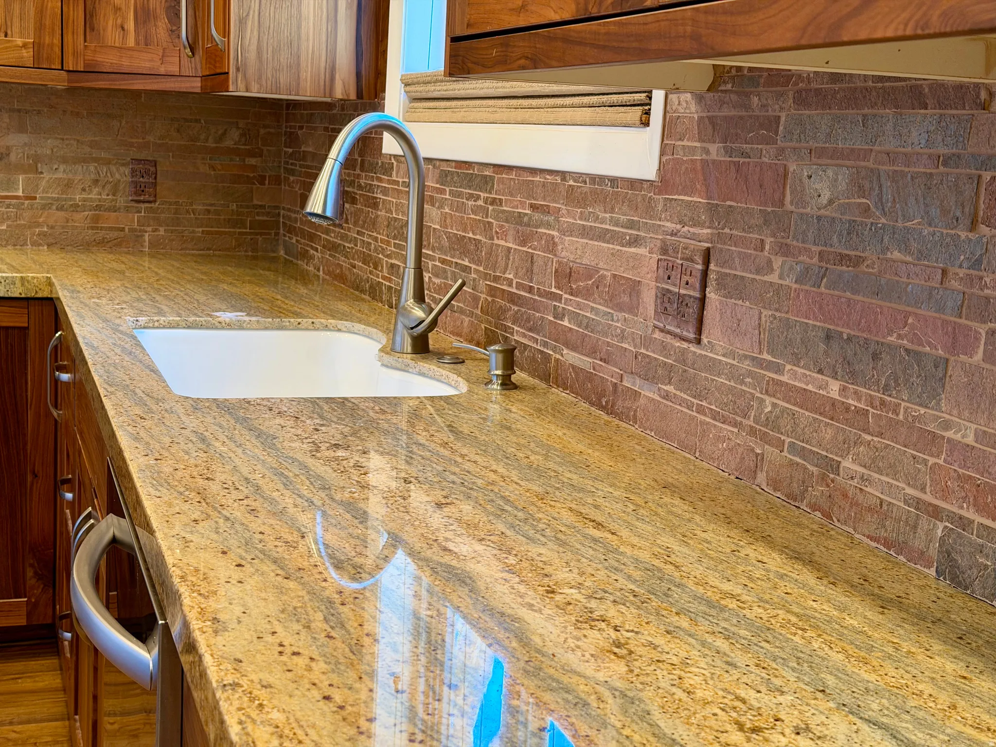 Kitchen view of light stone countertops, brown cabinetry, and stainless steel dishwasher