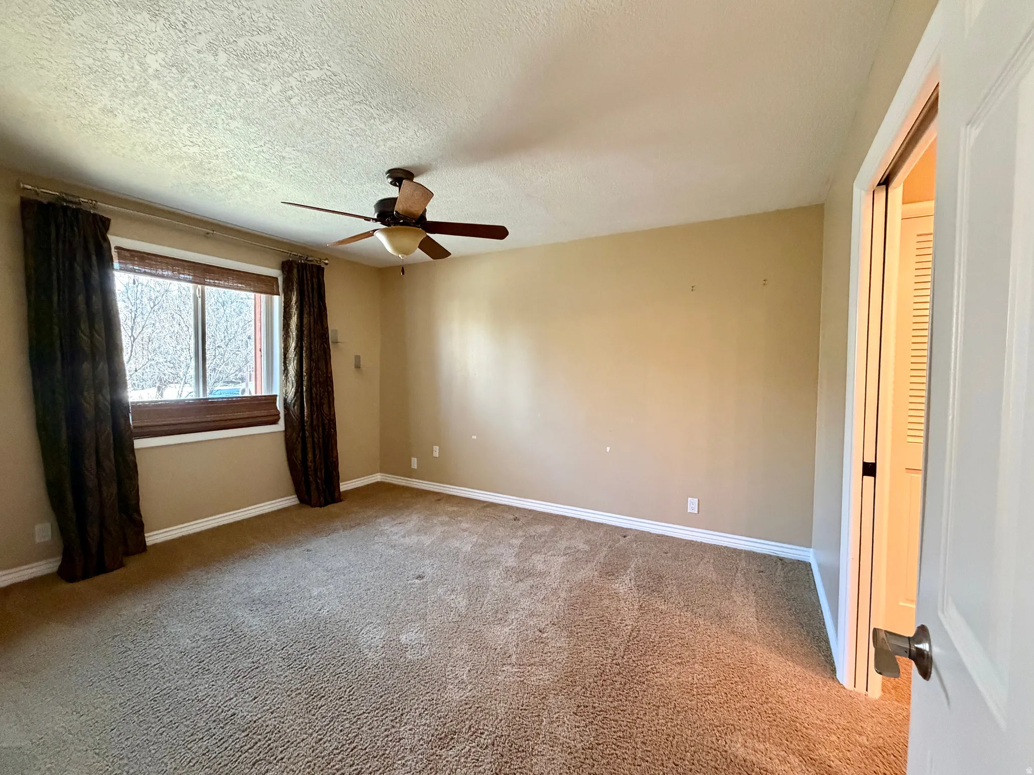 Empty room featuring carpet flooring, ceiling fan, and a textured ceiling